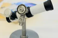 Tecnar by Swift 衛星望遠鏡。白い鏡筒に直角の接眼部、高度目盛環とコンパスを備えた灰色の鋳物台座。机の上に置いた全体